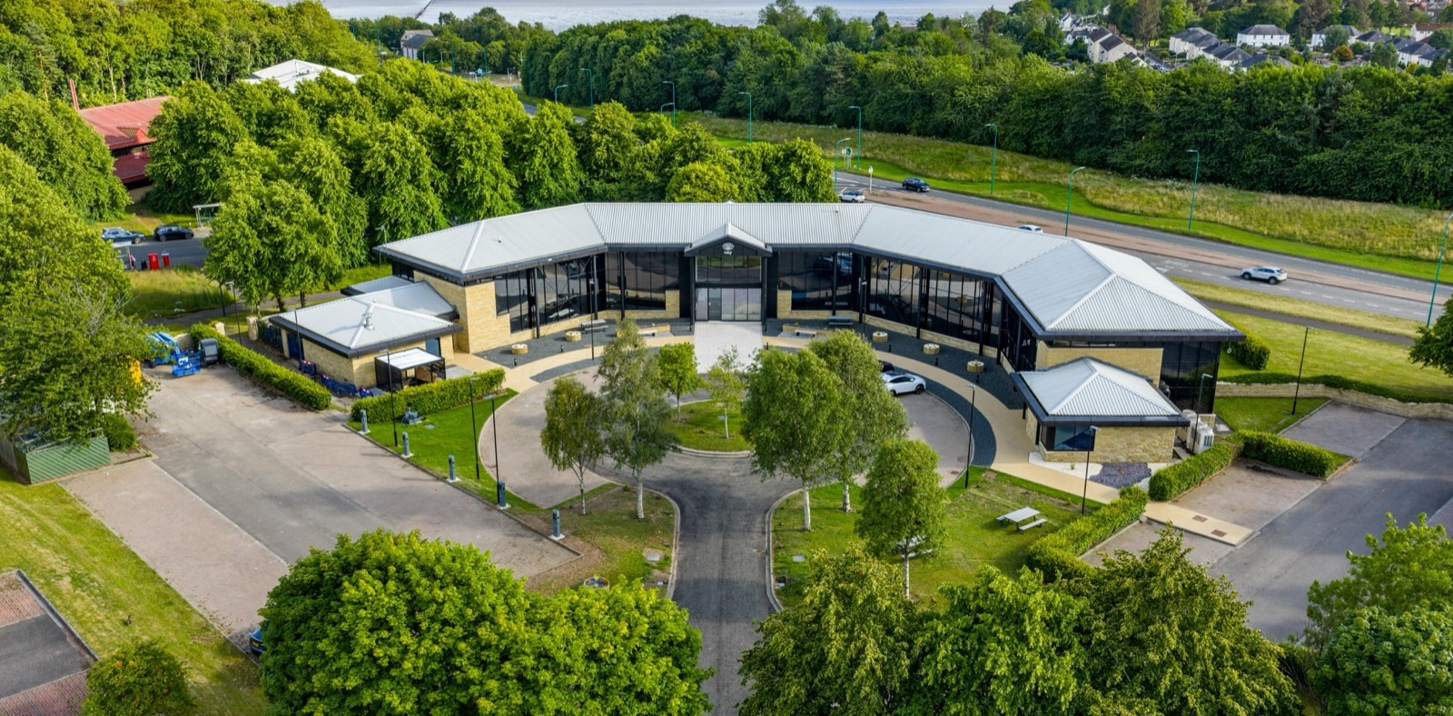 Aerial view of Ruby House, a low curved office building set among trees on Dundee Technology Park, with the Tay estuary beyond.